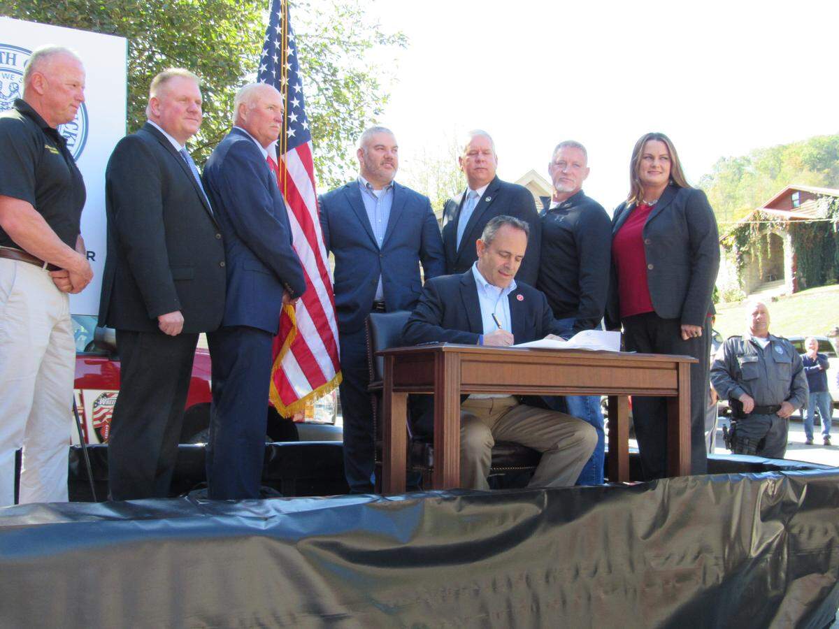 Gov. Matt Bevin, at the table, signs an order on Oct. 18, 2019 to house state inmates at a privately-owned prison in Floyd County as state and local officials look on.