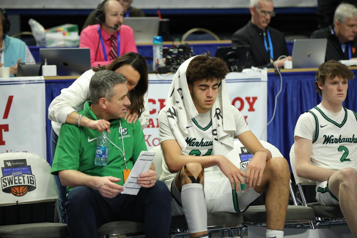 Great Crossing’s Malachi Moreno, center, reflected upon the Warhawks’ loss to Lyon County as head coach Steve Page, left, his wife, Tonya, and Ryan Payne (2) awaited the semifinalist trophy presentation after the Boys’ Sweet 16 semifinals on March 23. Moreno will be one of the favorites for the Kentucky Mr. Basketball award next year.