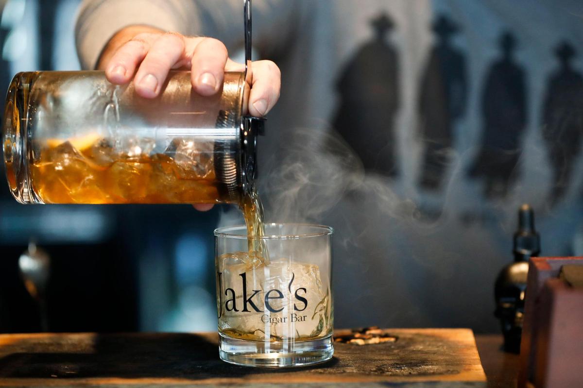 Bartender Cavanaugh Ragone pours a Smoked Old Fashioned made with a Knob Creek barrel pick. The cocktail is served in a glass lined with smoke from the wood of the barrel pick.