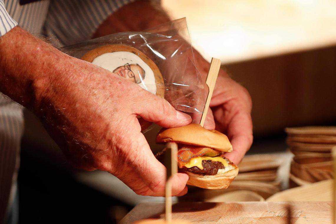 Rick Hilbert, of Wilmore, reaches for a cheeseburger slider and a cookie with Jim Gaffigan’s face on it In the new VIP Club at Rupp Arena Aug. 18, 2021.