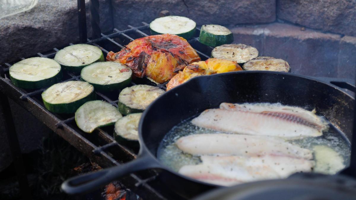 Cucumbers, tomatoes and tilapia cooks over a campfire on Tuesday, July 25, 2023 at Bourbon Barrel Cottages in Lawrenceburg, Ky.