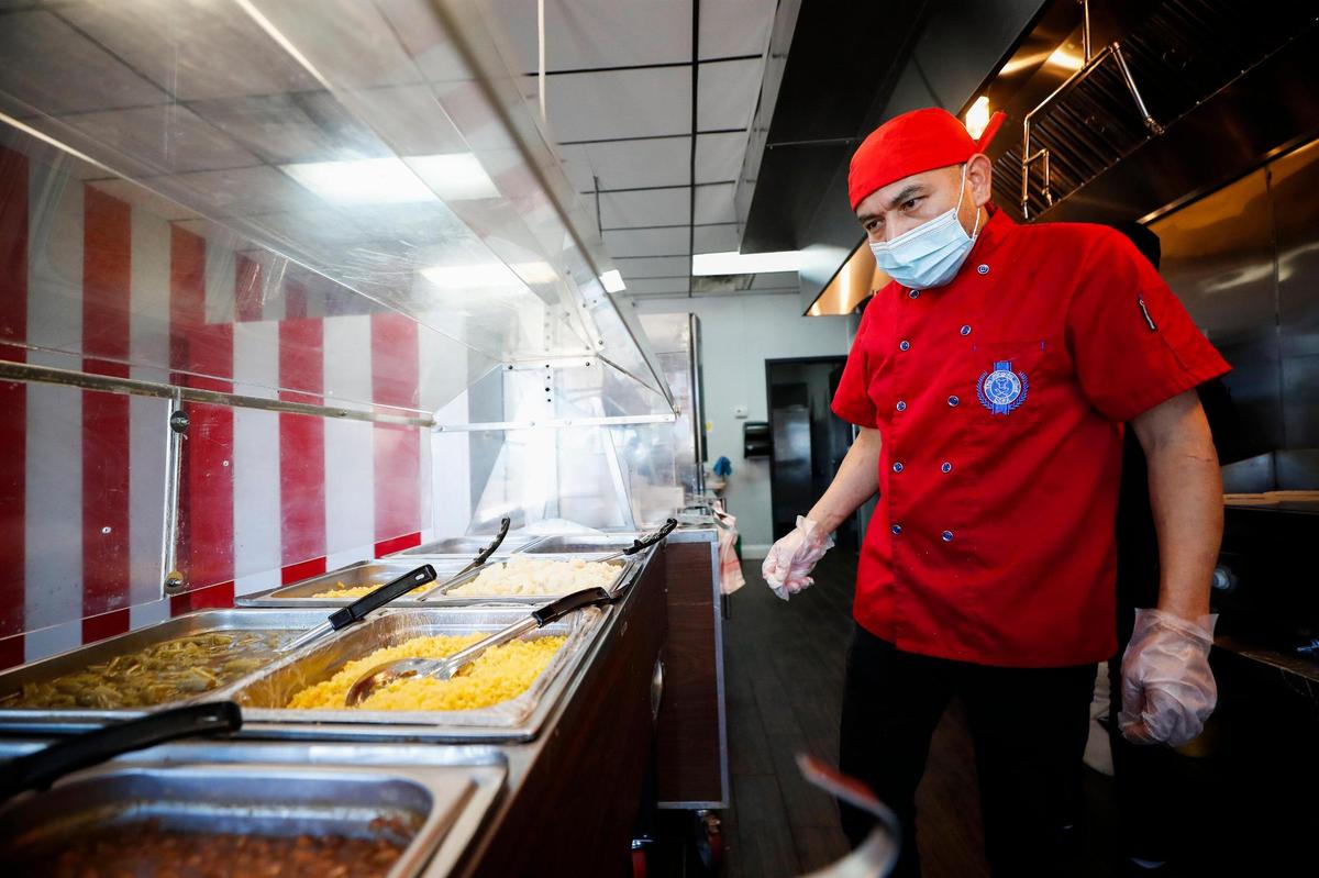 Alberto Geronimo, owner of Rosticeria Doña Coco examines trays of side dishes before customers arrive for lunch.