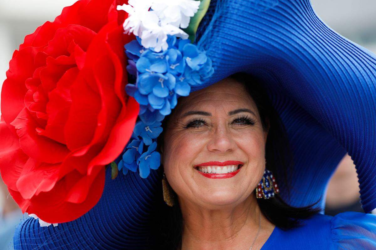 A woman in a large, bright hat featuring an oversized rose poses for a photo at Churchill Downs in Louisville, Ky., Saturday, May 6, 2023.