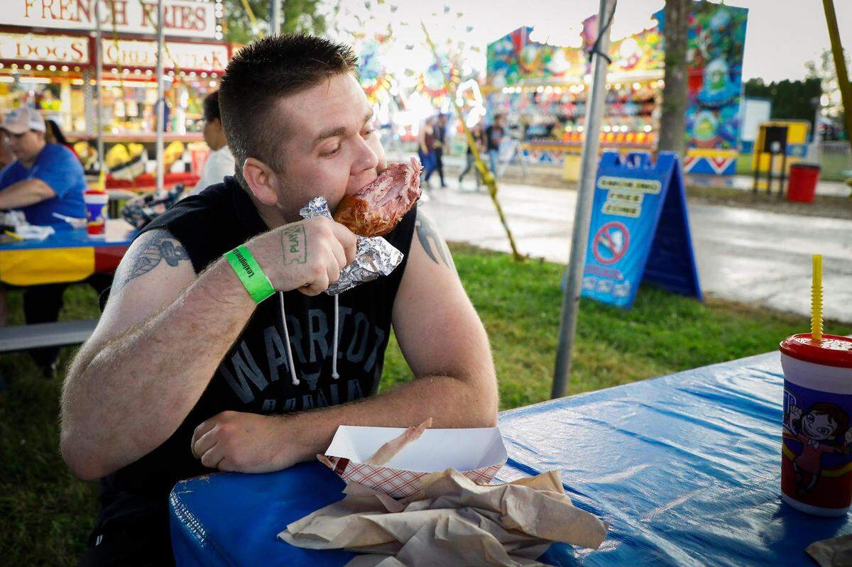Chris Hall, of Lexington, Ky., eats a turkey leg from Georges Fun Foods at the Lexington Lions Club’s Bluegrass Fair at Masterson Station Park in Lexington, Ky., Friday, June 11, 2021. Each leg is sugar cured and roasted for about 2 hours before being barbecue glazed and finished over charcoal.