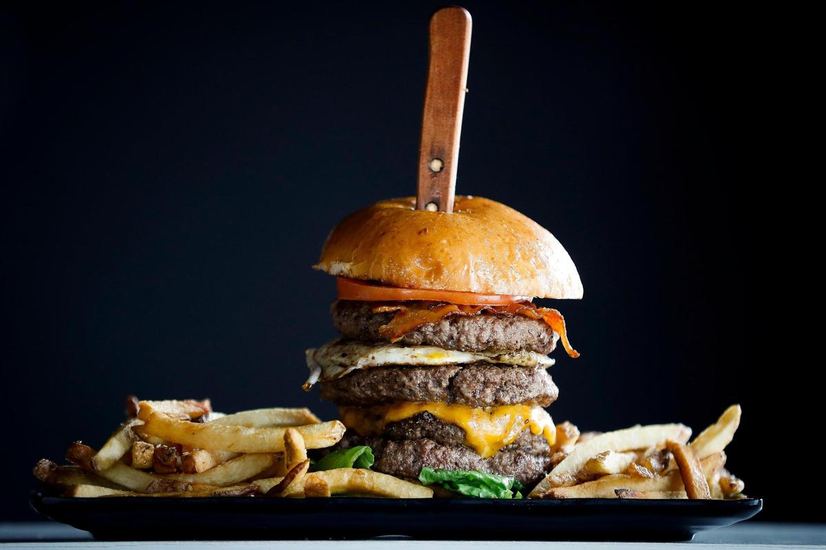 The Quadruple Bypass burger from Bad Wolf Burgers: four six-ounce seasoned beef patties, smoked bacon, a fried egg, cheese, garnished with lettuce and tomato and served on a brioche bun.
