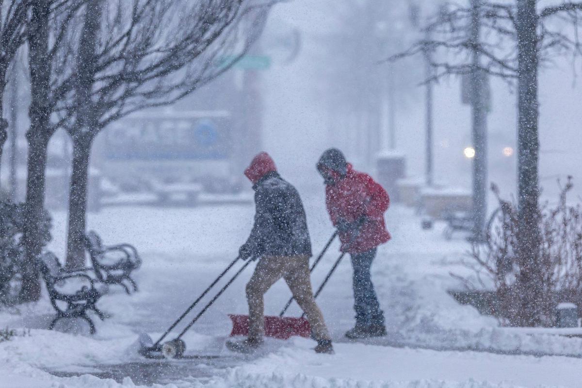 People clear snow from a sidewalk in downtown Lexington, Ky., on Sunday, Jan. 5, 2025.