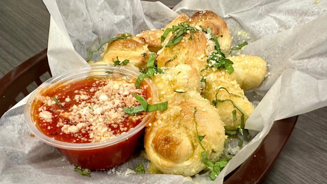 Garlic knots made with house pizza dough, knotted, baked and finished by tossing in garlic and extra virgin olive oil, peccorino romano, fresh basil and served with warm marinara at Ethereal Slice House.