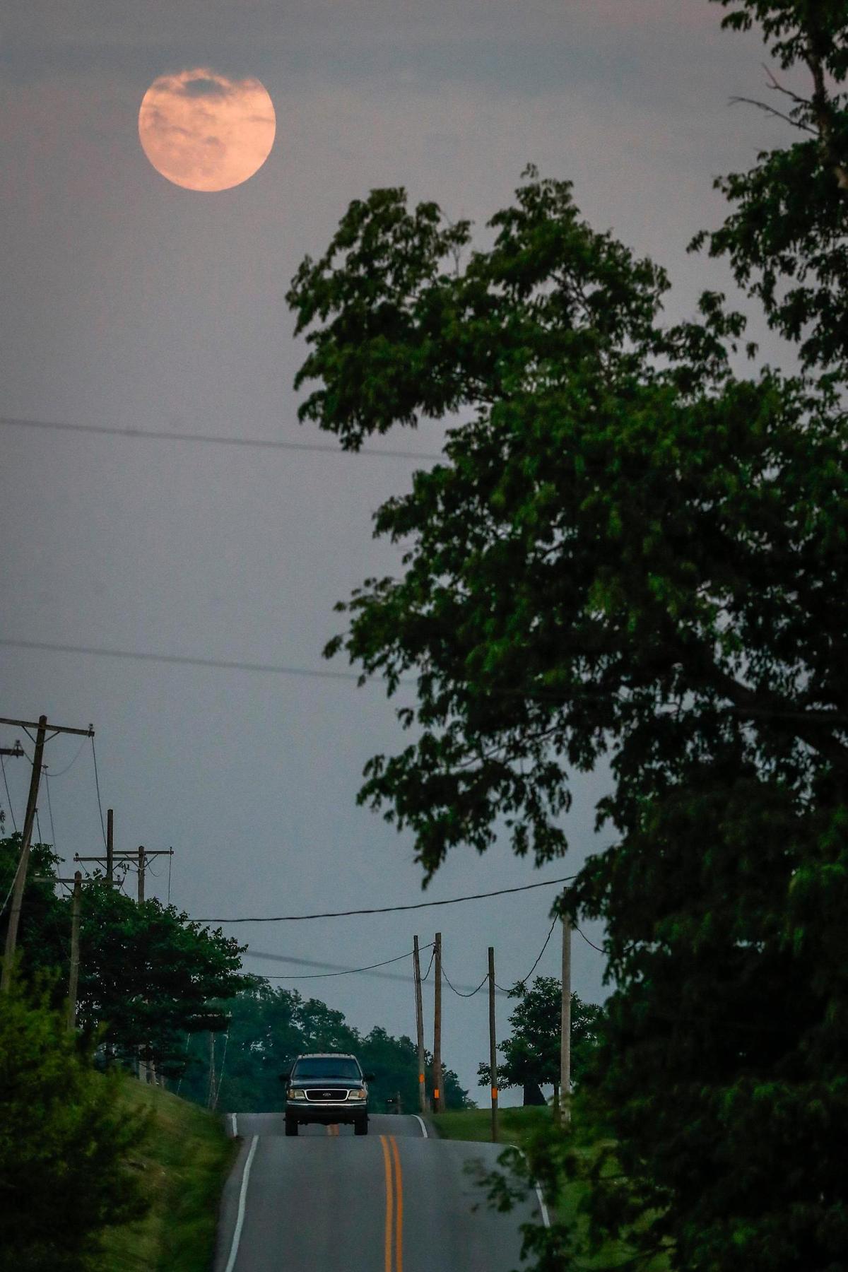 A motorists travels along Old Frankfort Pike Tuesday night as the Super Flower Blood Moon rises into view in Lexington.