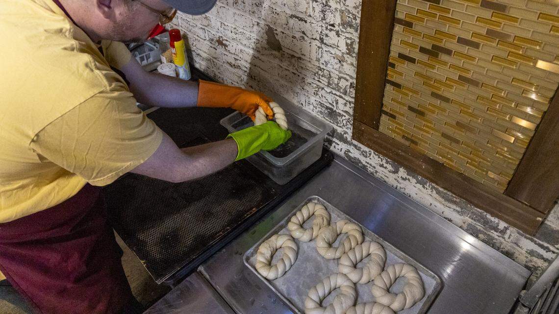 Jeremy Markle dips pretzels into a lye bath before they go into the over at The Wandering Bock Pretzel Pub & Brat Haus, Tuesday, March 24, 2026 in Lexington, Ky. Markle has to wear protective gloves while dipping the pretzels in the fresh lye (sodium hydroxide). The lye starts a chemical reaction on the skin of the pretzel and it gives it that brown, glossy crust when they bake.