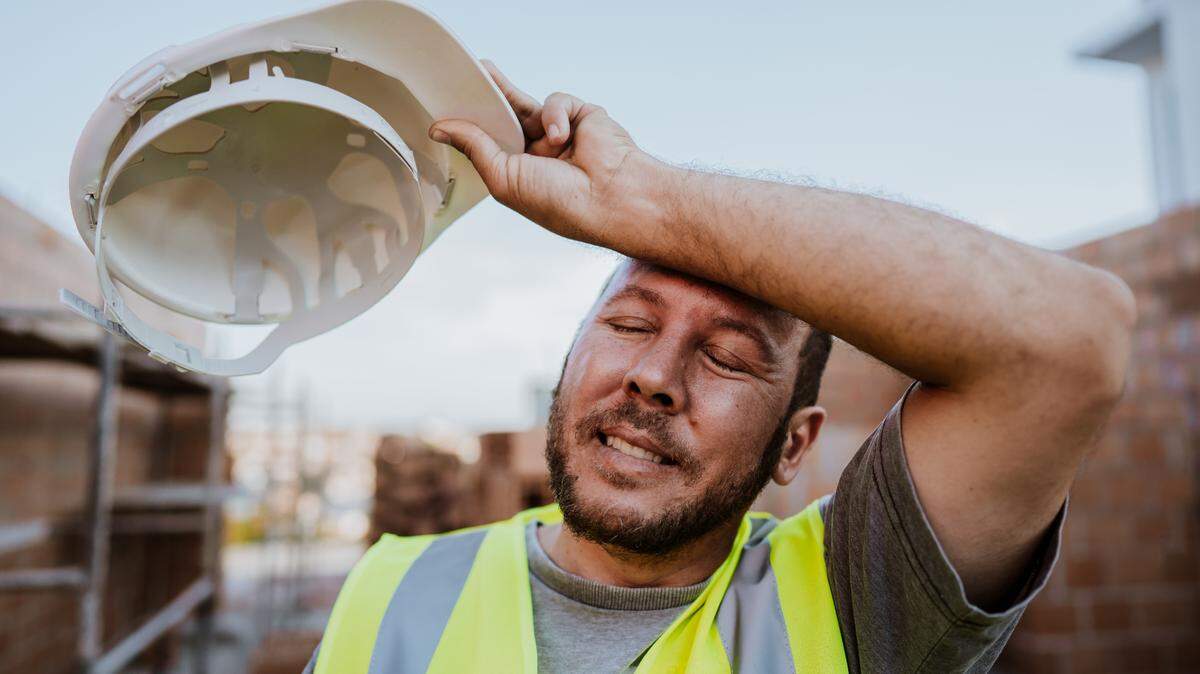 In this stock image, an exhausted construction worker wipes away sweat on a hot day.