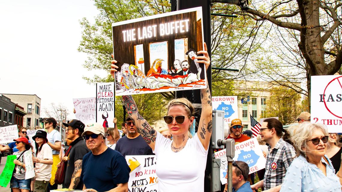 A protester holds a sign featuring President Donald Trump, cabinet members and constituents feasting on the remains of Lady Liberty as Da Vinci’s Last Supper during the “No Kings Then, No Kings Now” march and protest in front of the Robert F. Stephens Courthouse, in Lexington, Ky., April 19, 2025.