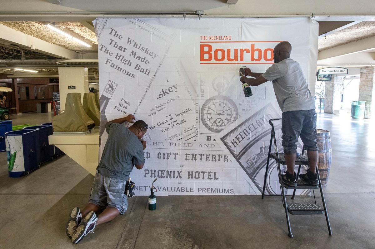 Steven Brown, left, and Anthony Adams, of Louisville-based JCGI Graphics and Imaging, apply a vinyl wall mural Wednesday for Keeneland’s new Bourbon Bar.
