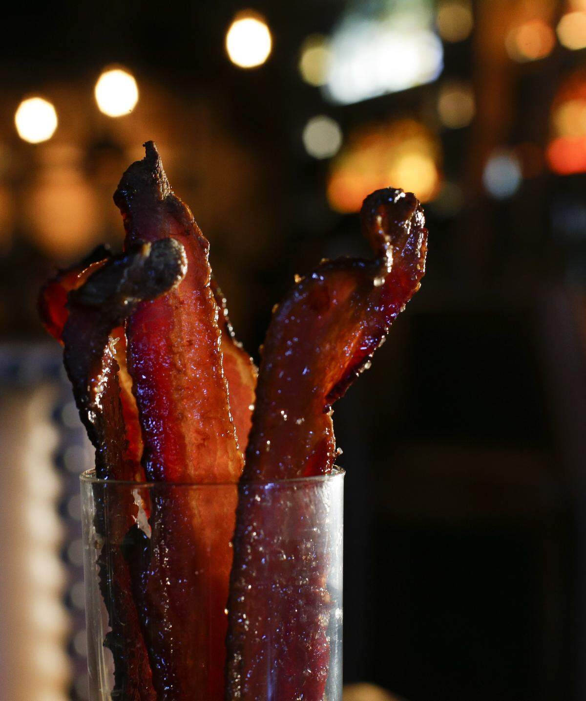 Bacon in a glass is glazed with honey and bourbon, caramelized, then served with melted peanut butter for dipping. 