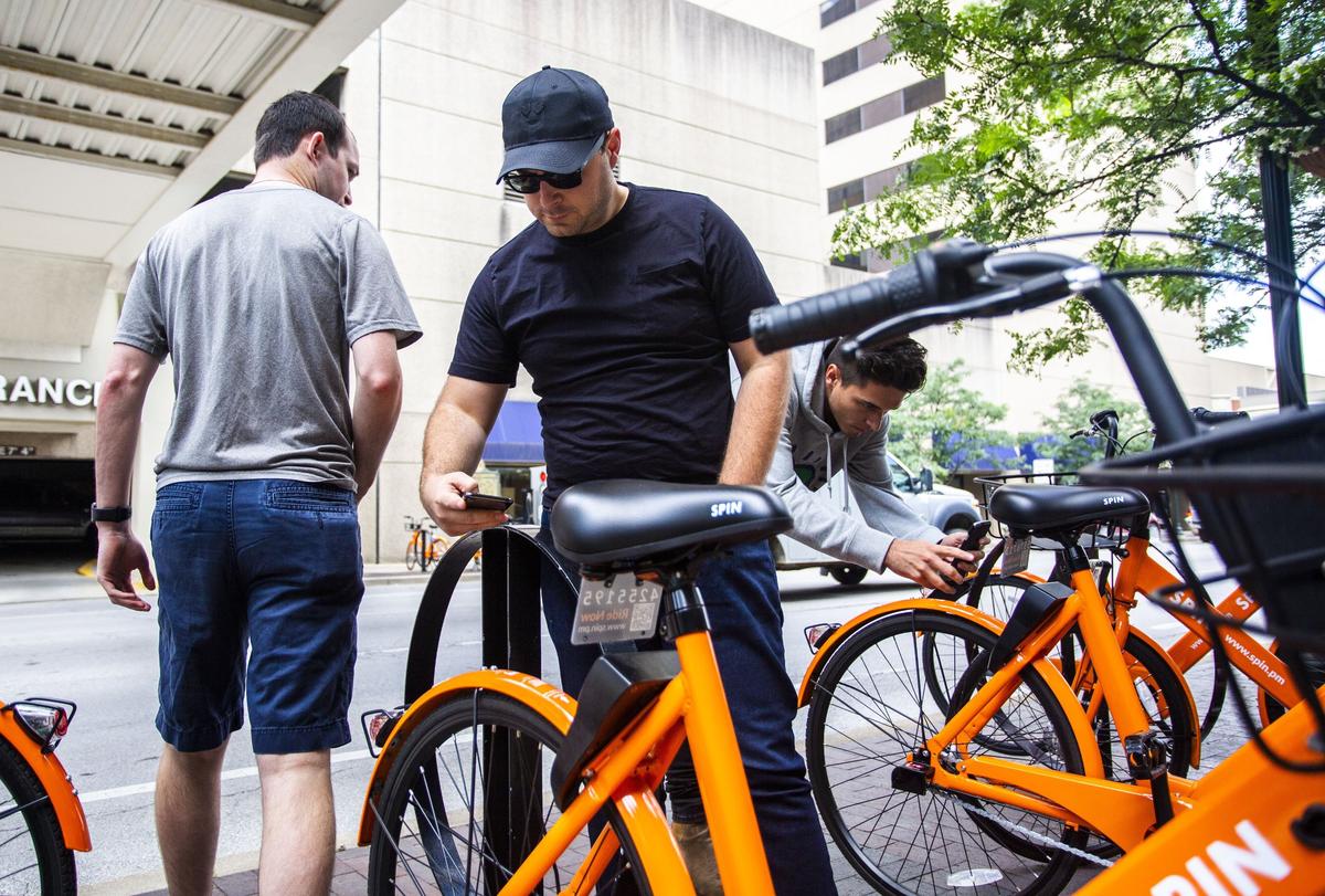 Gregg Morton, 30, scans the code on a Spin bike in downtown Lexington on Thursday afternoon. Spin launched a station-less bike system in Lexington on Monday. The bikes electronic components are charged by solar panels and do not require a rack system to charge.
