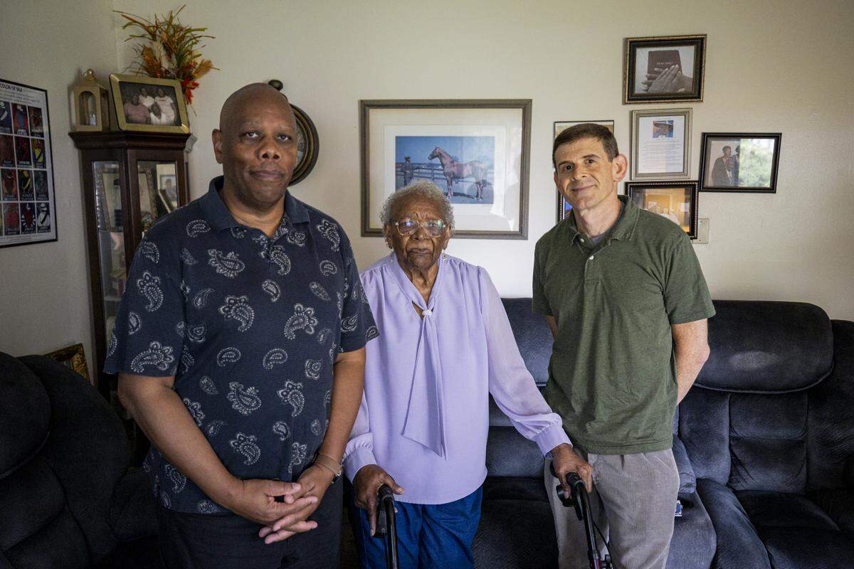 Kalvin Graves, left, Nora Williams, center, and Eli Scarr pose in front of the photo of Williams’ father, Cunningham Graves, when he was a groom of racehorse Man o’ War.