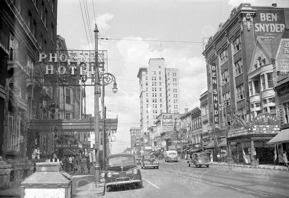 Downtown view of Lexington, looking west down East Main Street, cira 1944. On the left is the landmark Phoenix Hotel, which was demolished in 1981 and 1982 by Wallace Wilkinson, who planned to use the site to build the World Coal Center skyscraper. It was never built, and the site eventually became the Park Plaza Apartments and Phoenix Park. Up the right side is the Ben Ali Theater, which opened in 1913 at 121 East Main Street, across the street from the Phoenix Hotel. At four stories tall. It had a main auditorium, a balcony and a gallery, and 12 private boxes on each side, for a total seating capacity of 1,507. The floors had peacock-blue carpets with gold trim, and the walls were finished in ornamental plaster, with mosaic title floors and marble wainscoting. Built to house the top traveling play companies and grand opera, it was a vaudeville house in that medium’s heyday and again in the revival of the late 1940s and early 1950s. In its later days it showed movies, closing Sept. 9, 1964. Its last films were the James Bond movie “From Russia with Love” and “The Pink Panther.” It was torn town in 1965. Today it is the site of the Robert F. Stephens Courthouse Plaza. Next to the theater is the Ben Snyder department store. The store was founded in 1913 and had locations in Louisville, Paducah, Elizabethtown, Bowling Green and southern Indiana. This location operated from 1935 until 1980, leaving Wolf Wile’s as the only downtown Lexington department store.
