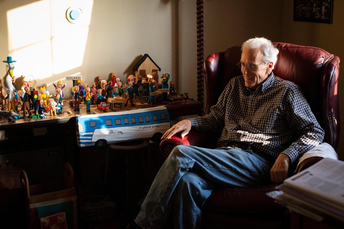Mike Norris sits next to a collection of wooden characters carved by Minnie Adkins in his Lexington home.