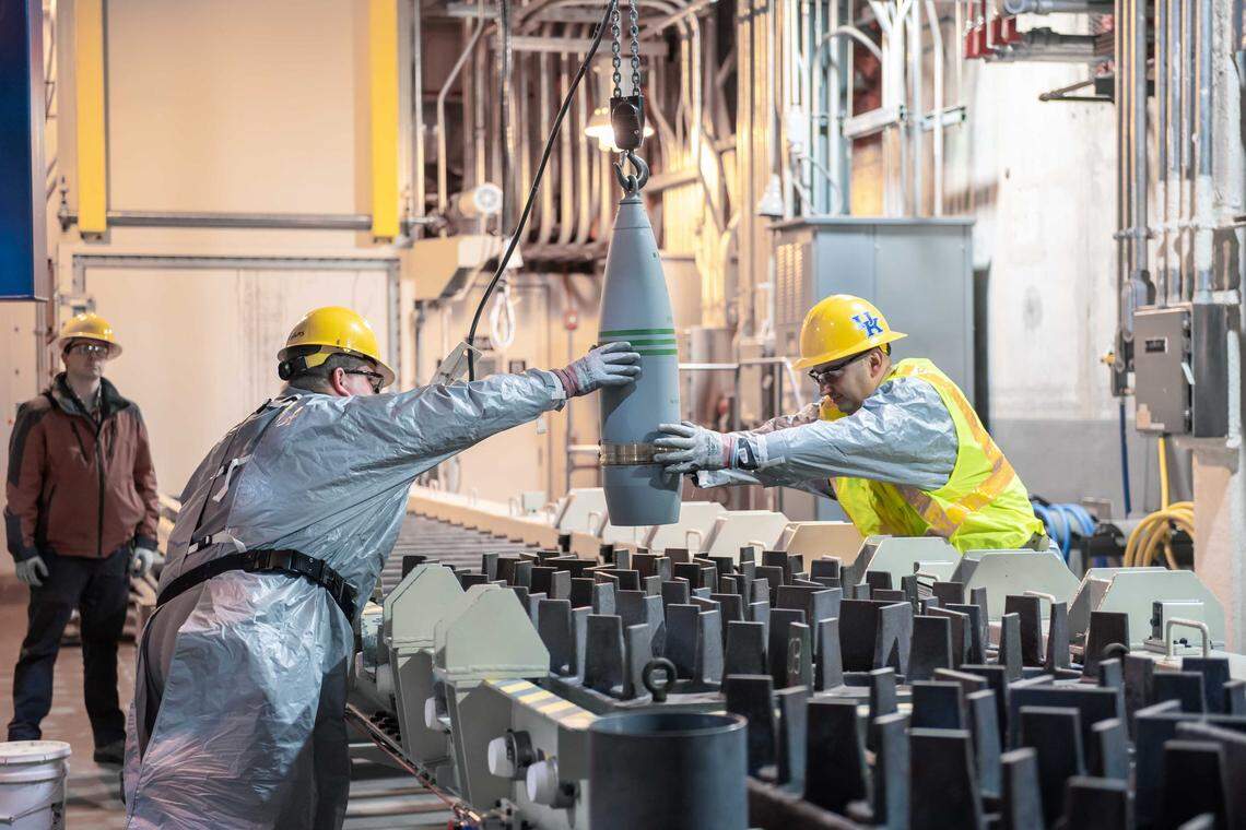 Blue Grass Chemical Agent-Destruction Pilot Plant workers place the first 8-inch projectile containing GB nerve agent or Sarin in a tray to begin the destruction process in the Munitions Demilitarization Building on Jan. 16, 2020.
