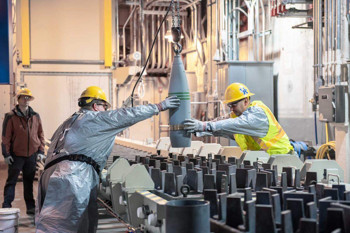 Blue Grass Chemical Agent-Destruction Pilot Plant workers place the first 8-inch projectile containing GB nerve agent or Sarin in a tray to begin the destruction process in the Munitions Demilitarization Building on Jan. 16, 2020.