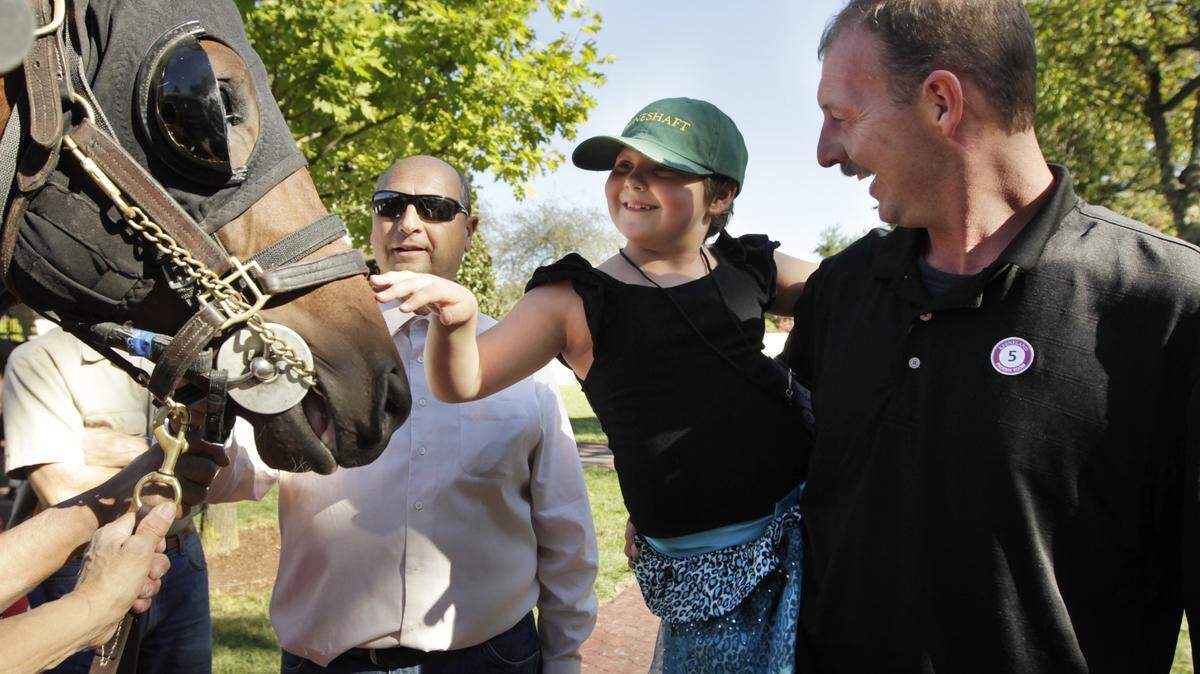 Cynthia Reitz, 8, of Maysville, petted Muppet Man with assistant trainer Jim Twardy, left, and her father, Nolan Powell, during Make-A-Wish Day at Keeneland on Thursday.