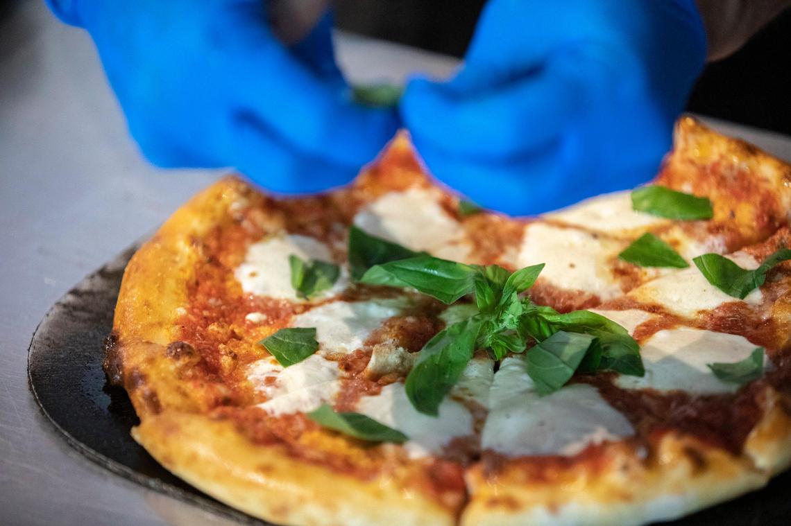 Sean Nealey, owner of PieTana, adds fresh basil Wednesday to a Margurite pizza at the restaurant at 210 Rosemont Garden.