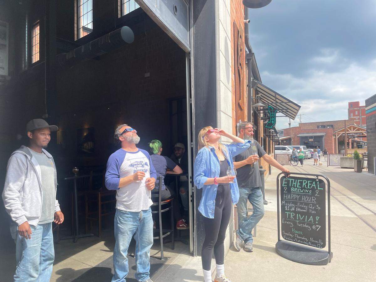 Haily Sloan (center) stands outside Ethereal Brewery in Lexington, Ky. to watch the solar eclipse April 8, 2024.
