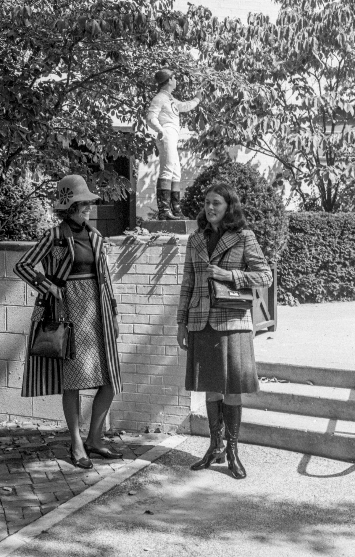 Mrs. Joseph A. Owens II, left, wears a blue and camel acrylic costume perfect for the changeable days of fall in the Blue Grass. The sleeveless top is blue and the skirt is coordinated with the pocket accent on the coat. With it she wears a camel felt hat with cutout detail, pointing to the return this fall of the real hat. Her costume is from Meyers. Mrs. Charles Nuckols III, selects a double-breasted plaid blazer with charcoal flannel skirt and matching knit top from McAlpins’s. The costume was designed by Kasper for Joan Leslie. 