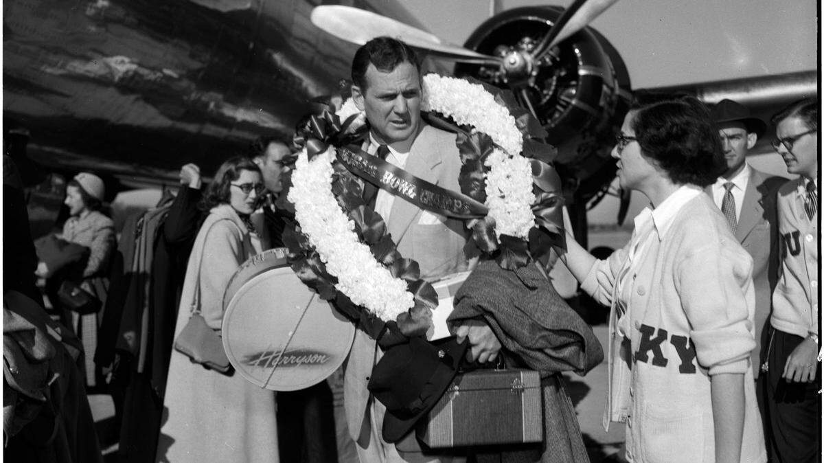 As soon as he stepped of a plane Jan. 5, 1951 at Blue Grass Field, University of Kentucky football coach Paul “Bear” Bryant received a wreath of roses around his neck. Four days earlier in New Orleans, his Cats upset No. 1 Oklahoma in the Sugar Bowl. After being greeted at the airport, the team boarded buses, and was escorted by city, county and state motorcycle patrolmen down crowd-lined streets to Memorial Coliseum. There they were honored before 9,000 fans and presented the Sugar Bowl trophy. The crowd and University President Dr. Herman Lee Donovan lauded Bryant, who cautioned everyone that their first game on next year’s schedule was just around the corner. Bryant coached at Kentucky for eight winning seasons from 1946 to 1953 before leaving for Texas A&M. He later went to Tuscaloosa and was the legendary coach of Alabama for 25 years, leading the Crimson Tide to six national titles. Published in the Lexington Leader January 5, 1951. Herald-Leader Archive Photo