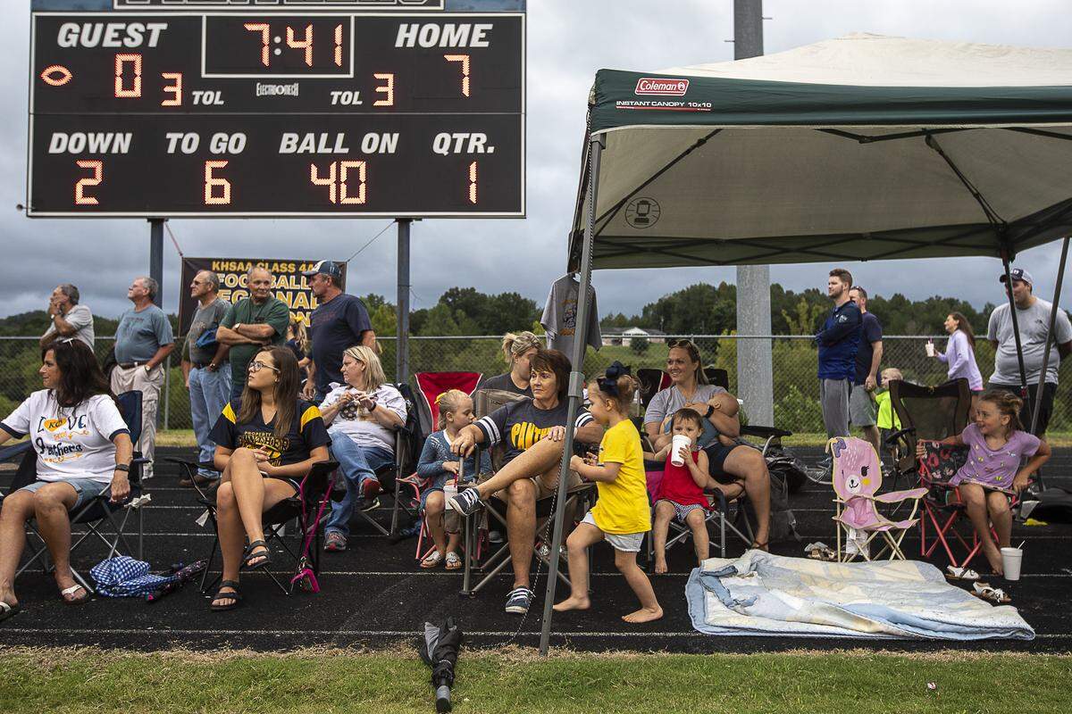 Fans watch the game from chairs and canopies set up along the track surrounding the field.