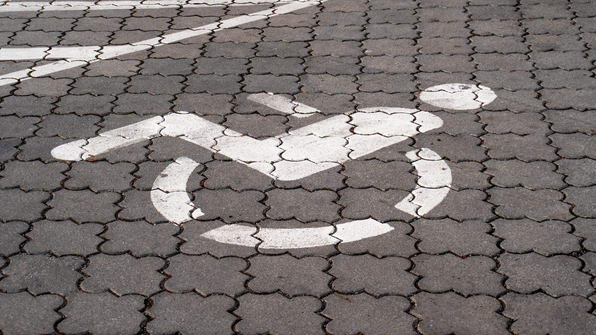 A stock photo displays an accessible parking space, marking with a picture of a person using a wheelchair.