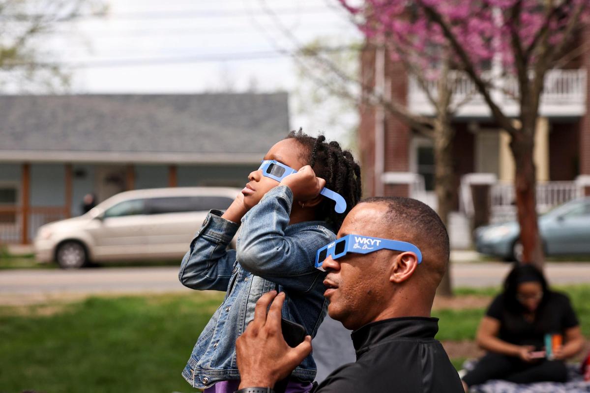 Dr. Lezell Lowe holds his granddaughter, Niyeah, as people gather to view a total solar eclipse seen from the Living Arts & Science Center in Lexington, Ky., Monday, April 8, 2024.