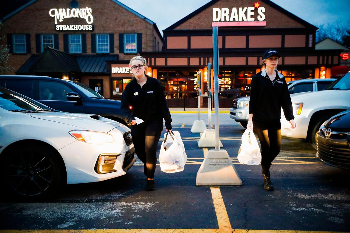 Whitney Powell left, and Emily Mink deliver take out orders to customers Saturday in the parking lot of Malone’s Lansdowne. All orders at Malone’s and Drake’s will be delivered to customers curbside.