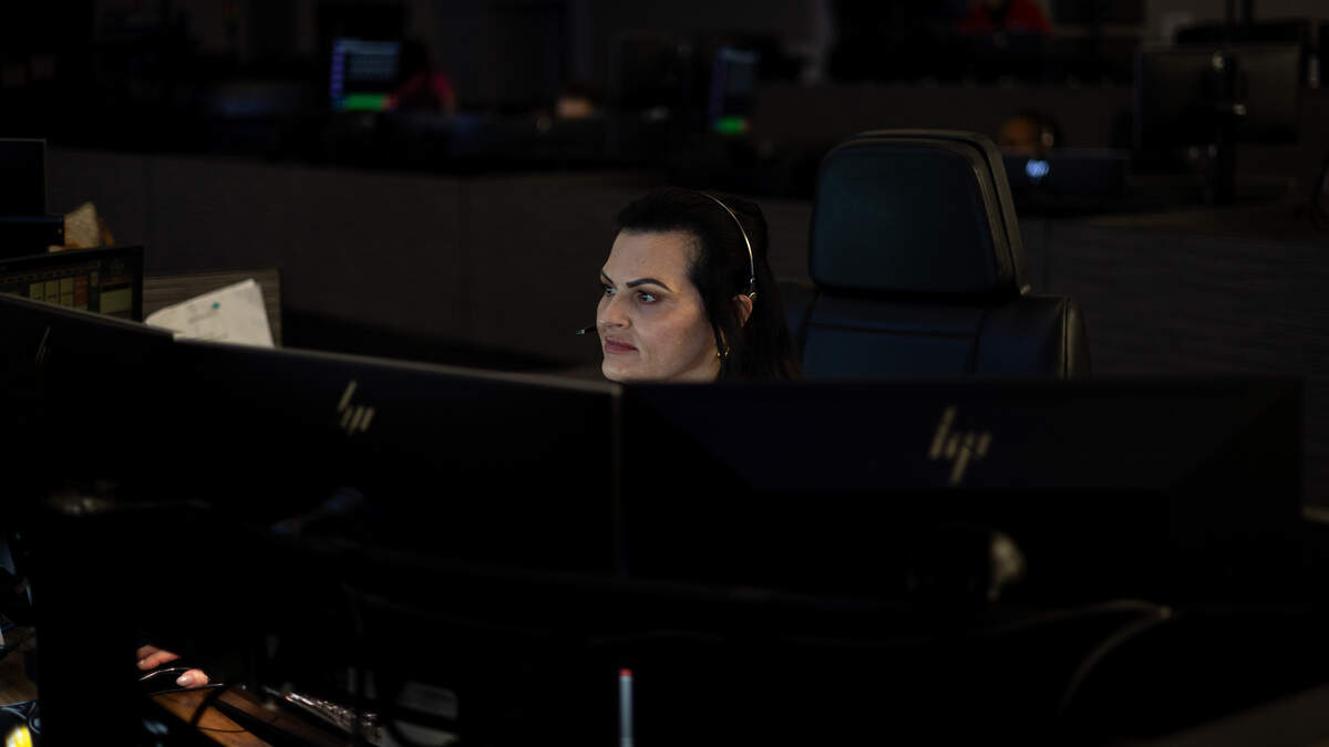 A woman sits in front of monitors that shine onto her face in a call canter.