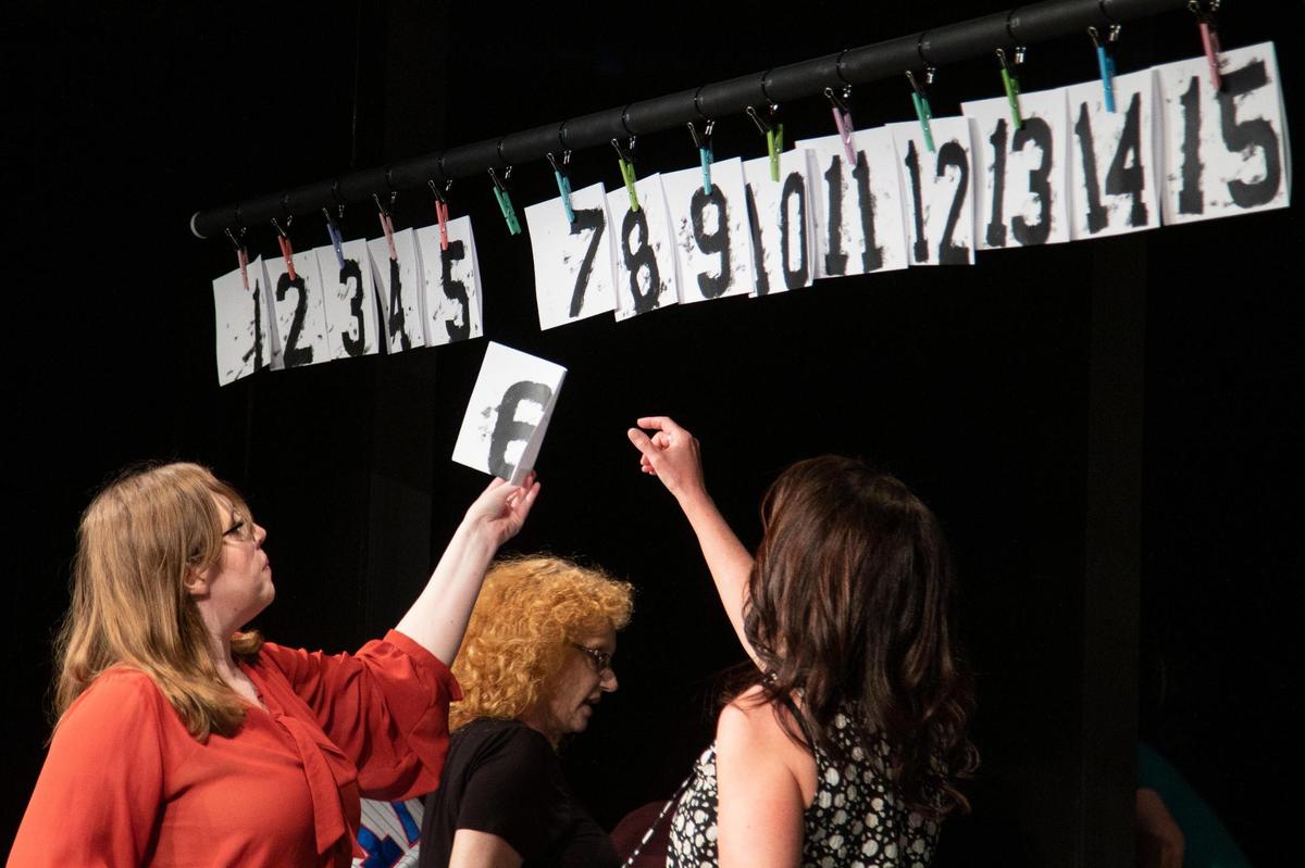 Ellie Hudd removes a numbered play from its position over the stage after an audience members shouted out the number during a dress rehearsal of “Too Much Light Makes the Baby Go Blind” at the Carriage House in Lexington, Ky., Tuesday, May 10, 2022. The order of plays is chosen at random from pieces of paper hanging over the stage.