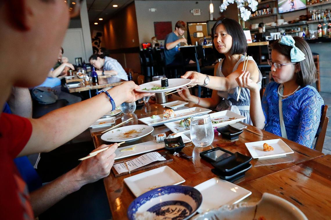 Hui-Nee See Tyler, of Lexington, Ky., center, hands a piece of sushi to her son Jonas Tyler, 15, also of Lexington, at Zen Sushi & Sake in Lexington, Friday July 26, 2019. Over the past year the Tyler family have been eating “alphabet dinners” choosing restaurants from a-z staring with Asian Wind and ending with Zen Sushi & Sake.