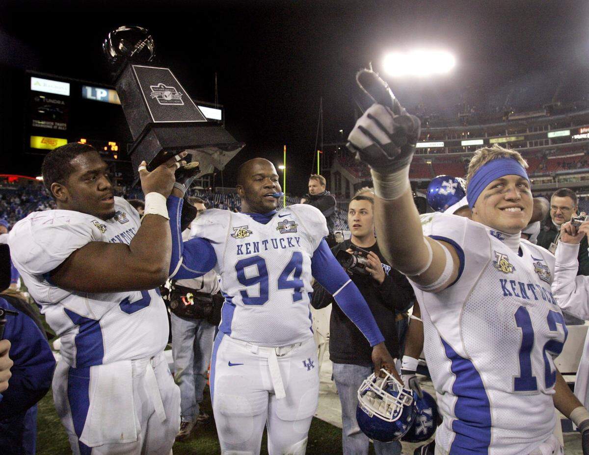 Kentucky center Eric Scott, left, hoisted the trophy with defensive end Travis Day (94) as wide receiver Dicky Lyons (12) pointed to fans after the Cats defeated Florida State in the 2007 Music City Bowl.