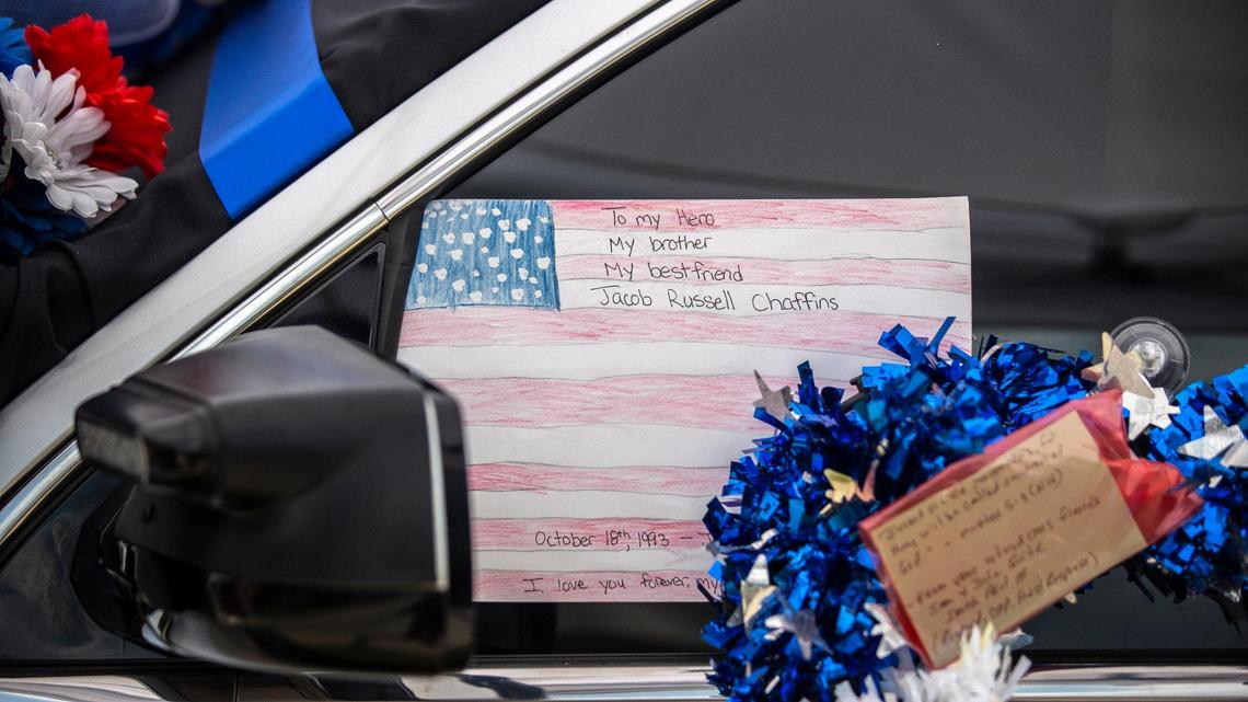 Flowers, cards and signs honoring three Floyd County law enforcement officers killed in the line of duty cover a police car parked in front of the municipal building in Prestonsburg, Ky., July 7, 2022. A mural honoring the officers was vandalized this week, police report.
