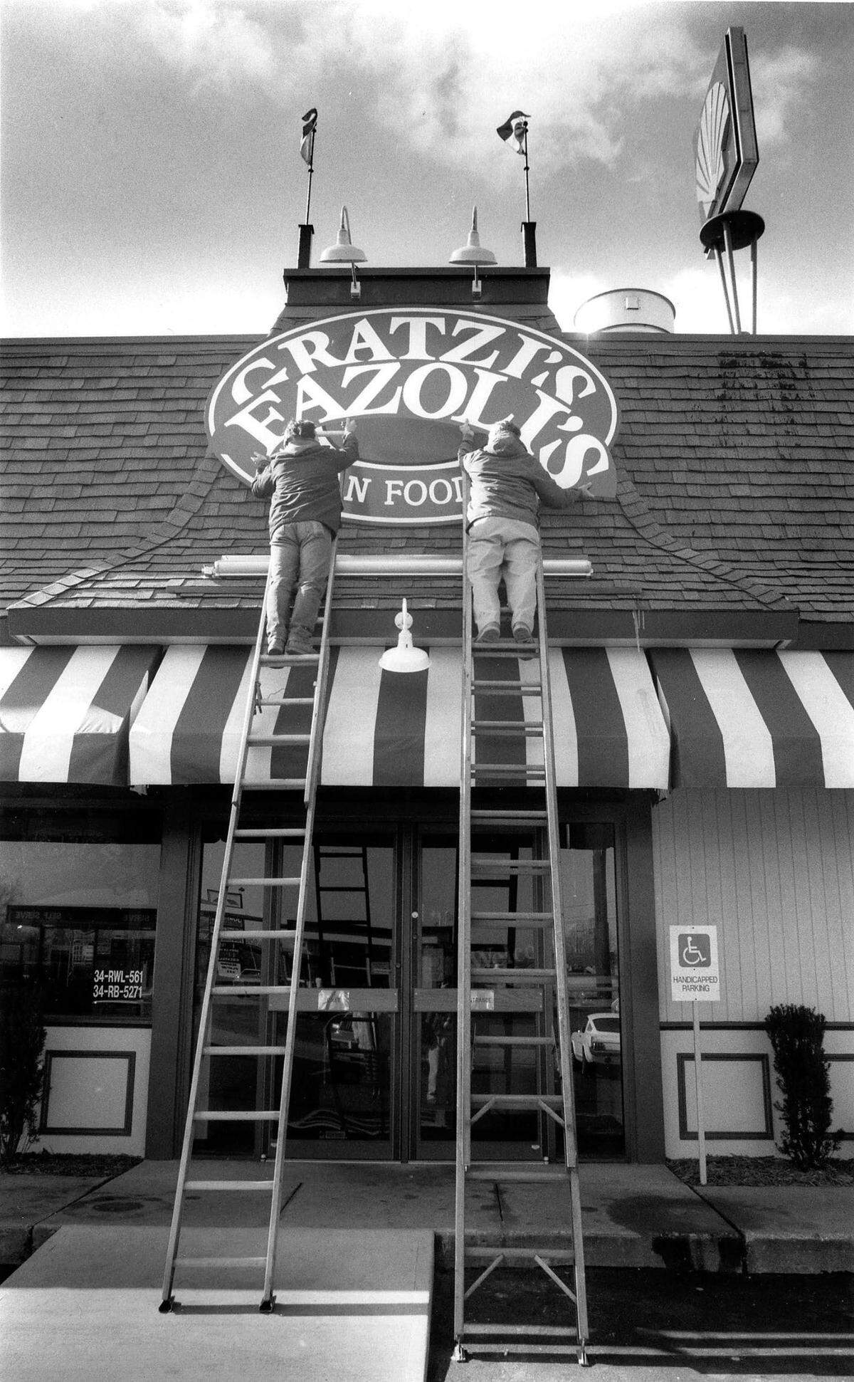 Martin Sherrod, left and Clint Sherrod of the Sherrod Sign Company change the sign on Gratzi’s, on North Broadway in Lexington, to it’s new name, Fazoli’s, February 10, 1989. 