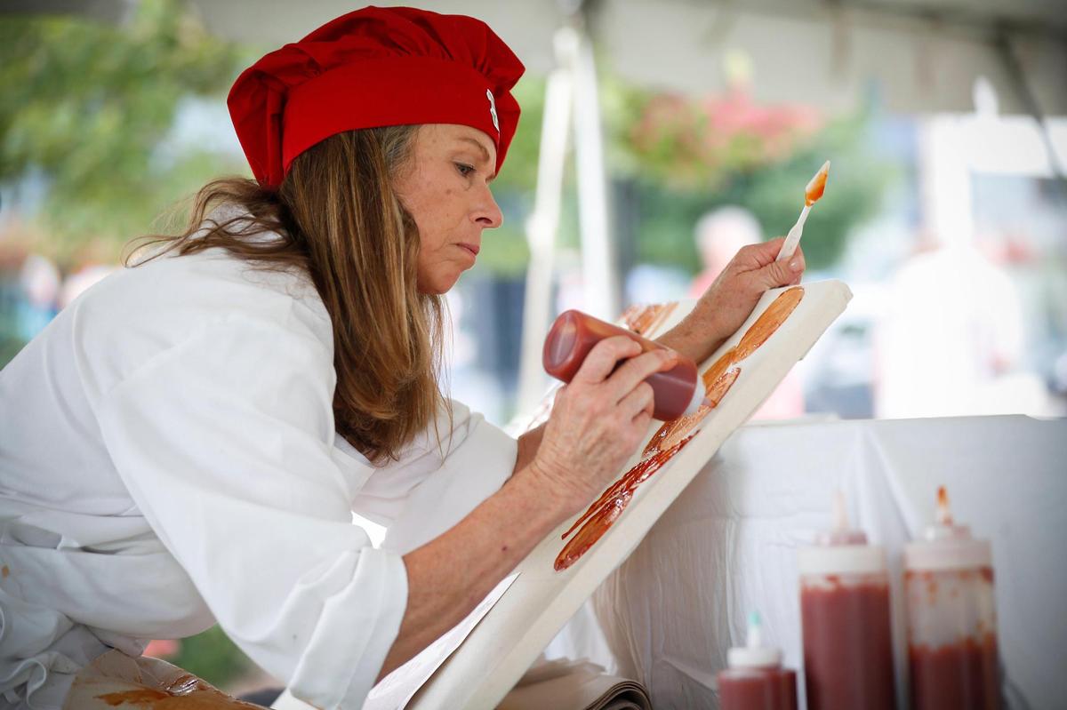 Cynthia Kostylo, of Lexington, Ky., paints with Heinz ketchup during Ketchup Art on the Green at The Summit at Fritz Farm in Lexington, Saturday, July 31, 2021. Kostylo says that ketchup is a similar medium to standard paint but the final product is temporary, “So it’s just playing with food,” She said.
