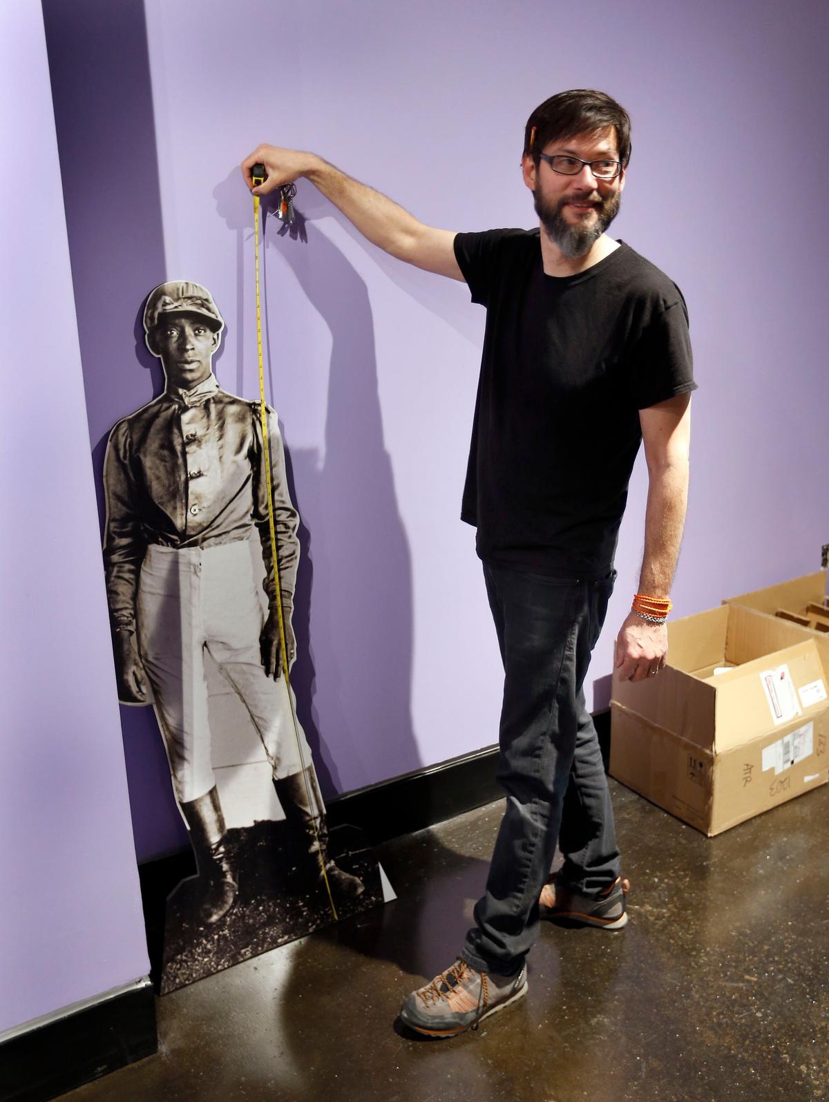 James Shambhu measured the height of a photo of jockey Jimmy Winkfield at the Kentucky Horse Park Black Horsemen of the Turf exhibit located in the International Museum of the Horse at the park on Iron Works Road. This exhibit was the last exhibit done by museum director Bill Cooke before he retired.