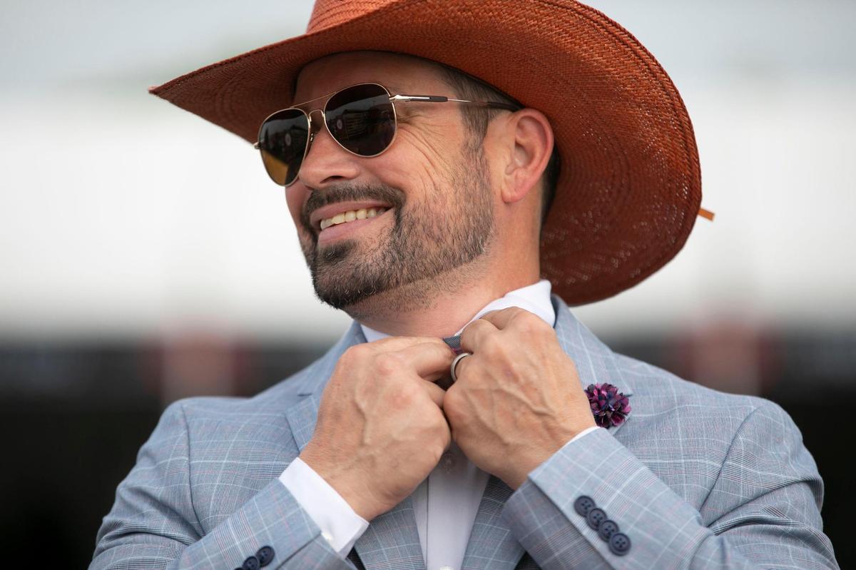 Brian Rennolds fixes his bowtie at Churchill Downs in Louisville, Ky., Saturday, May 6, 2023. He purchased his burnt orange hat for the Kentucky Derby from a Lexington hat shop.