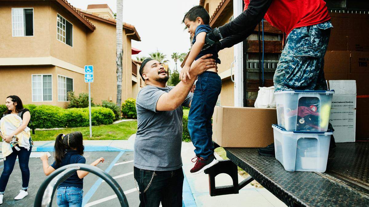 In this stock image, a mover hands a young boy to his father from back of moving truck.