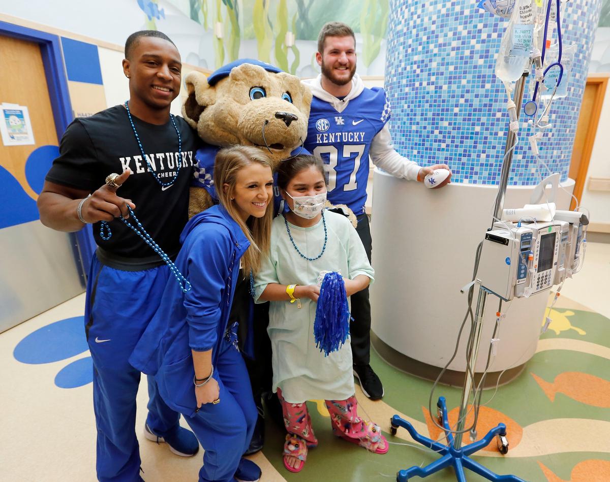 University of Kentucky cheerleaders Josh Marsh and Riley Aguiar, Wildcat mascot Scratch, and UK football player C.J. Conrad had their photo taken with 12-year-old patient Adriana Juarez-Torres as the group visited with patients Tuesday morning in the Kentucky Children’s Hospital.