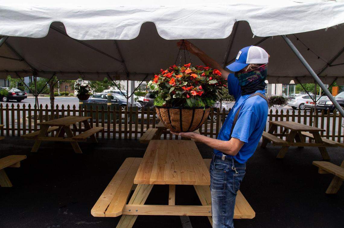 Mack Herndon hangs a flower basket to decorate the new tent that is up at Epping’s on Eastside on July 28 the day after Gov. Andy Beshear’s announcement of further restrictions on restaurant capacity due to COVID-19. The tent allows Epping’s to serve more customers. Pemberton’s Greenhouse, the family business where Herndon works, has been working closely with local restaurants to ensure that their outdoor seating arrangements still feel purposeful and distract from the fact that these pop-up outside seating arrangements are often in parking lots.