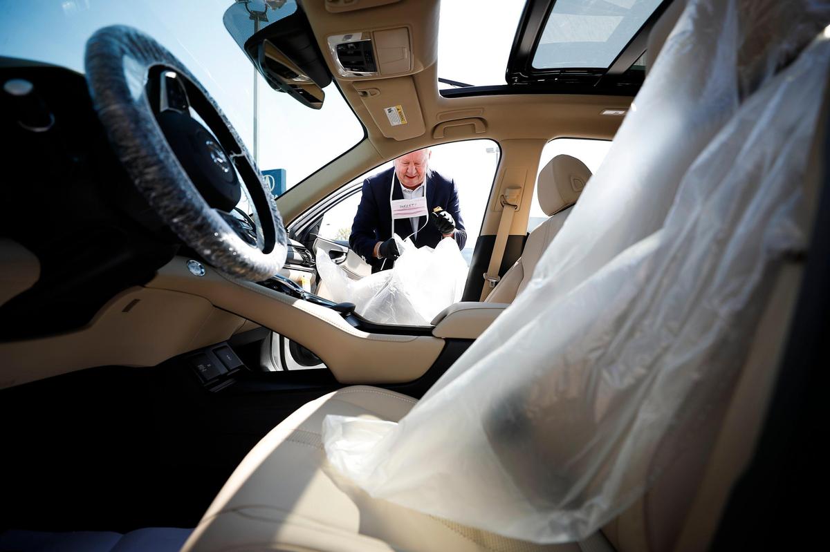 Dan Glass, vice president and general manager at Courtesy Acura, demonstrates applying protective plastic covers to seat inside of a car Saturday at Courtesy Acura in Lexington. All cars are being cleaned and sanitized before being driven by customers.