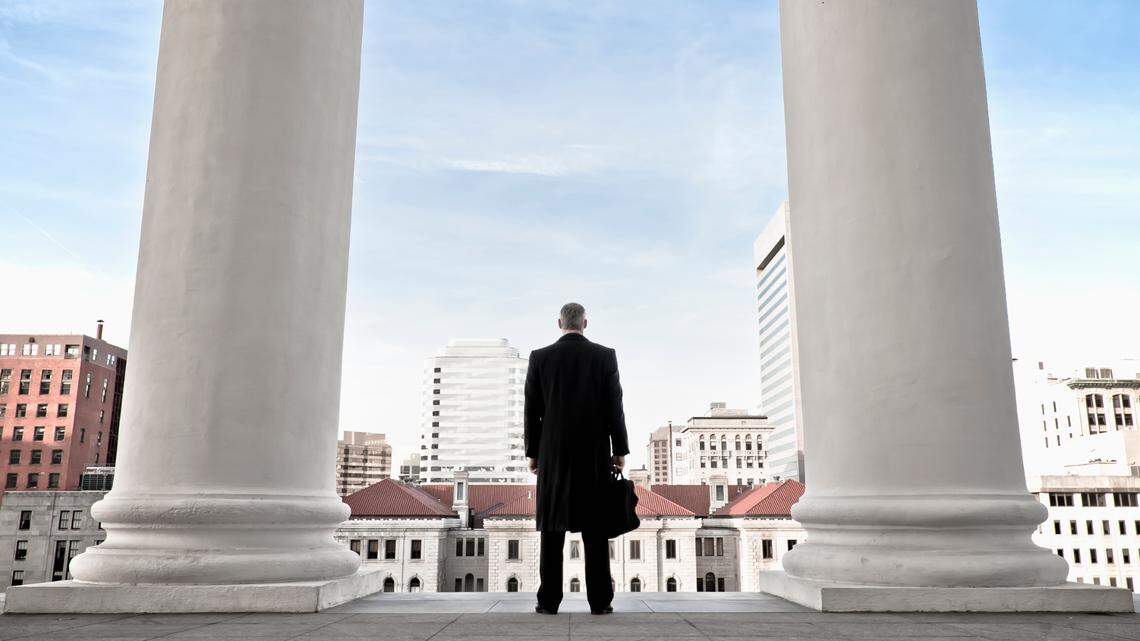 A businessman looks out at a cityscape as he stands between two columns.