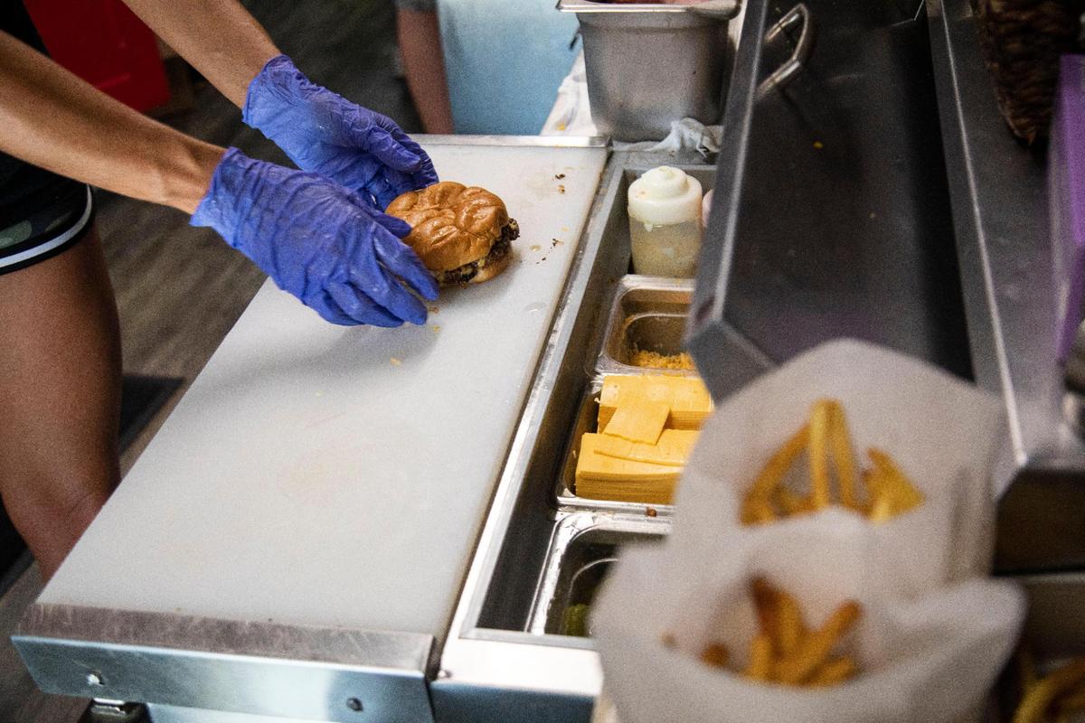 Assistant manager Laken Burchett prepares a burger July 10 at the Drive-In restaurant in Olive Hill. The restaurant also features sliders and the Baby Henri (named after Antrobus’ youngest son) which has a a small two-ounce patty.