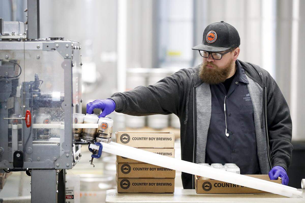 Jake Mulert, of Lexington, grabs cans of Shotgun Wedding as they come off of the canning line at Country Boy Brewing in Georgetown.