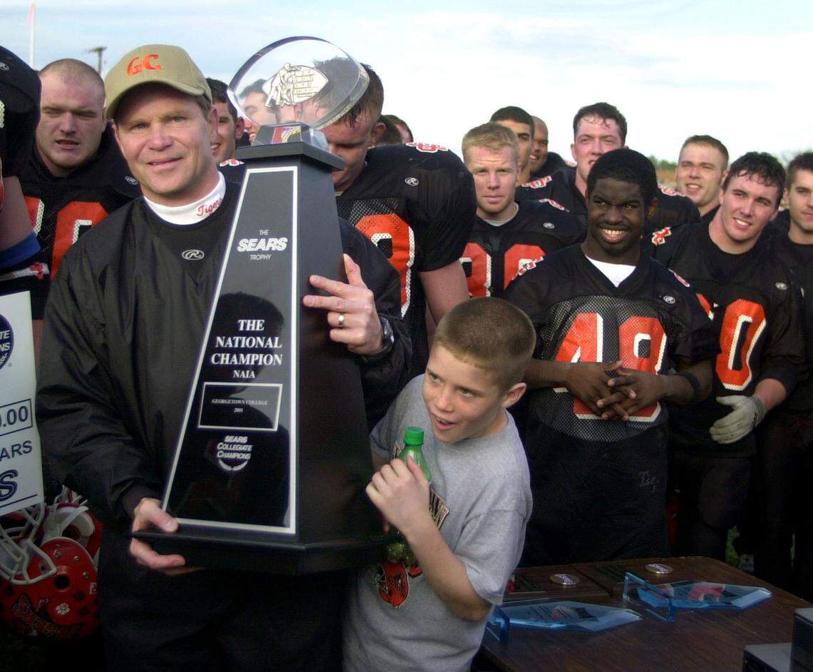 Bill Cronin holds the NAIA championship trophy as his son, Cory, 10, tries to get a better look after Georgetown won its second national title under Cronin at Savannah, Tenn., in 2001. “You never accomplish the things you do alone,” Cronin said upon announcing his retirement Monday.