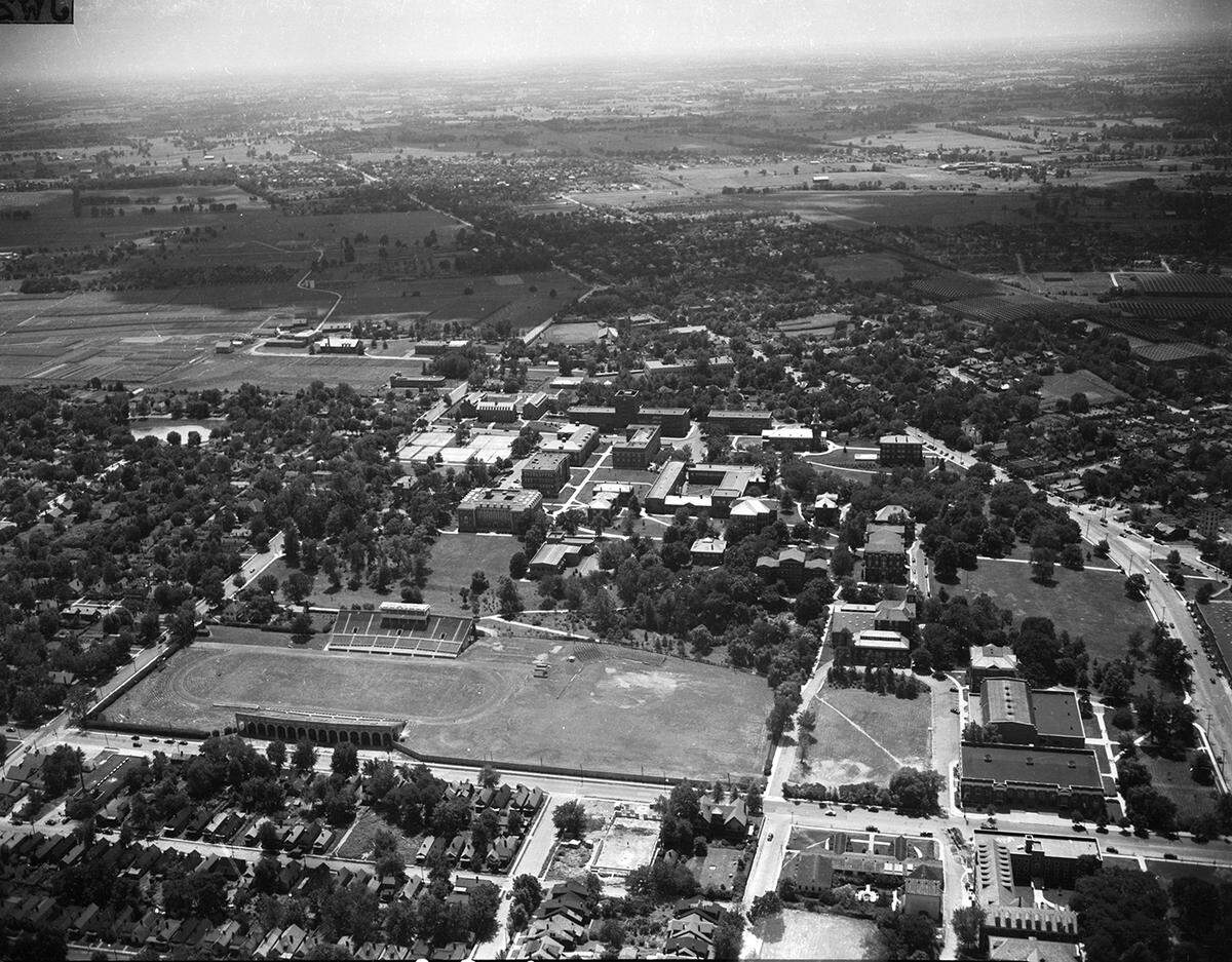 This is an aerial view of the University of Kentucky campus around 1945-1946. What is now Avenue of Champions runs left to right near the bottom of the photograph with Stoll Field and McLean Stadium, center, lower left. It was the home of the University of Kentucky Wildcats football team. The field had been in use since 1880, but the concrete stands were opened in October 1916 and closed following the 1972 season. It was replaced by Commonwealth Stadium, now called Kroger Field. This photograph was taken prior to Memorial Coliseum, which was built in 1950.